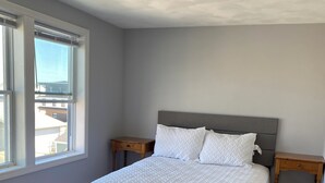 A bedroom with a large bed, a nightstand, a dresser, and a window with blinds.