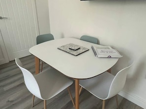 Una mesa de comedor pequeña y redonda con mantel blanco, dos sillas blancas y un cuaderno sobre la mesa.