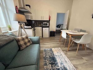 Un espace de vie compact comprenant un canapé, une table à manger avec des chaises, un coin cuisine et un petit réfrigérateur.