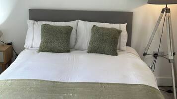 Un lit avec une tête de lit grise, une literie blanche et deux coussins verts.