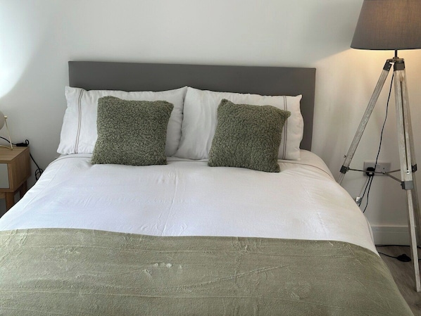 Una cama con cabecera gris, ropa de cama blanca y dos almohadas verdes.