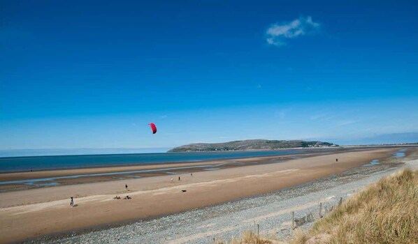 Una playa con cielo despejado, una colina distante y una persona volando una cometa.
