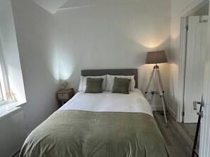 Een slaapkamer met een bed, nachtkastje, lamp en een raam.