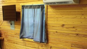 A room with a bed, a wooden wall, a mounted TV, and an air conditioning unit.