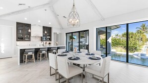 A modern kitchen with a large island, white cabinetry, and a dining area with a round table and chairs. - Bella Fratelli Marco Island 🏝️
With Electric Lift Pier (Marco Island)
