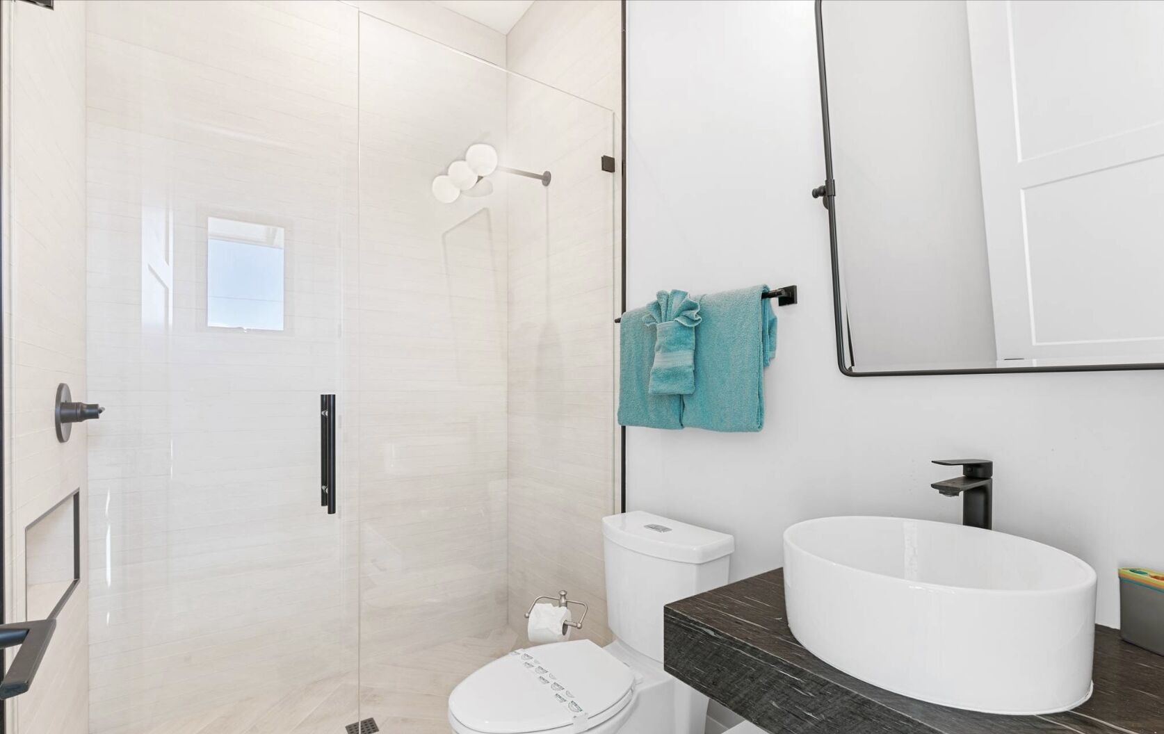 Ein modernes Badezimmer mit einer gläsernen Dusche, einer weißen Toilette, einem großen weißen Waschbecken und einem Handtuchhalter mit einem blauen Handtuch.