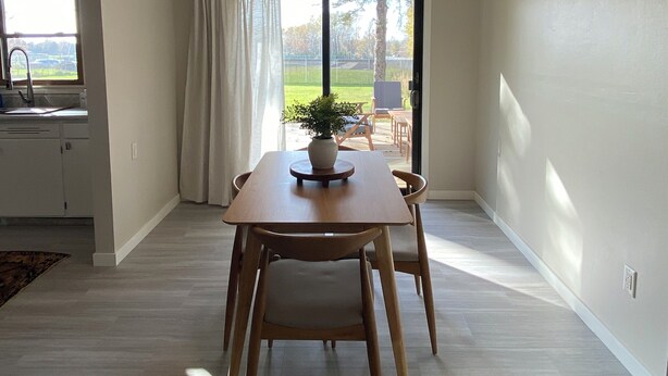 Un área de comedor con una mesa y sillas, una planta en maceta y vistas al exterior a través de un ventanal.