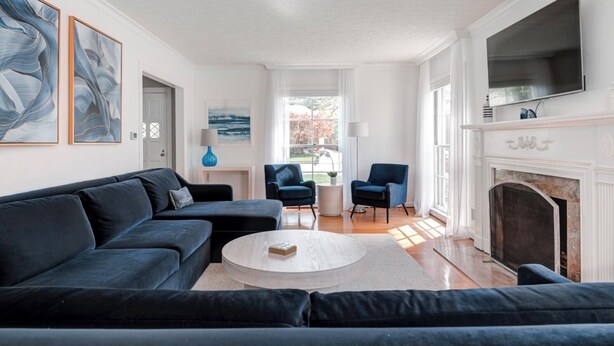 Una sala de estar moderna con un sofá modular, una mesa de centro redonda y una chimenea. Hay dos sillones y una lámpara sobre una mesita auxiliar.