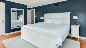 Un dormitorio con una cama grande, mesitas de noche blancas, un ventilador de techo y un espejo en la pared.