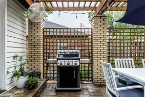 A patio with a grill, potted plants, and a table with chairs.