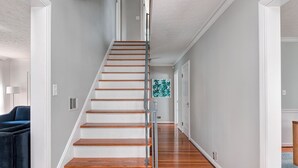 Una escalera de madera con barandilla metálica que conduce a una habitación con un sofá azul y una obra de arte colgada en la pared.