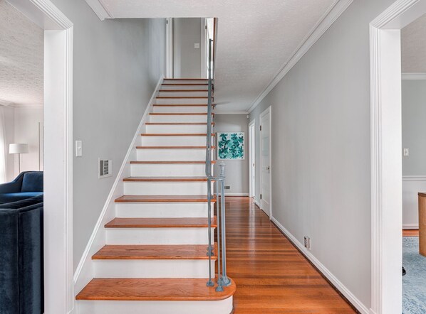 A staircase with wooden steps and a metal handrail, leading to a room with a blue couch and a wall-mounted artwork.