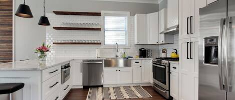 A modern kitchen with white cabinetry, stainless steel appliances, and a wooden floor.