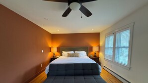 A bedroom with a bed, two bedside tables, a ceiling fan, and a window with blinds.
