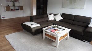 A modern living room with a dark brown sofa, a white coffee table with magazines, and a white rug. - Sedan16 Zentral (Wuppertal)
