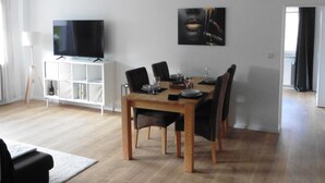 A dining area with a wooden table set for four, a television on a white cabinet, and a painting on the wall. - Sedan16 Zentral (Wuppertal)