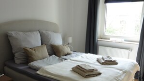 A modern bedroom with a large bed, a bedside table, and a window with curtains. - Sedan16 Zentral (Wuppertal)
