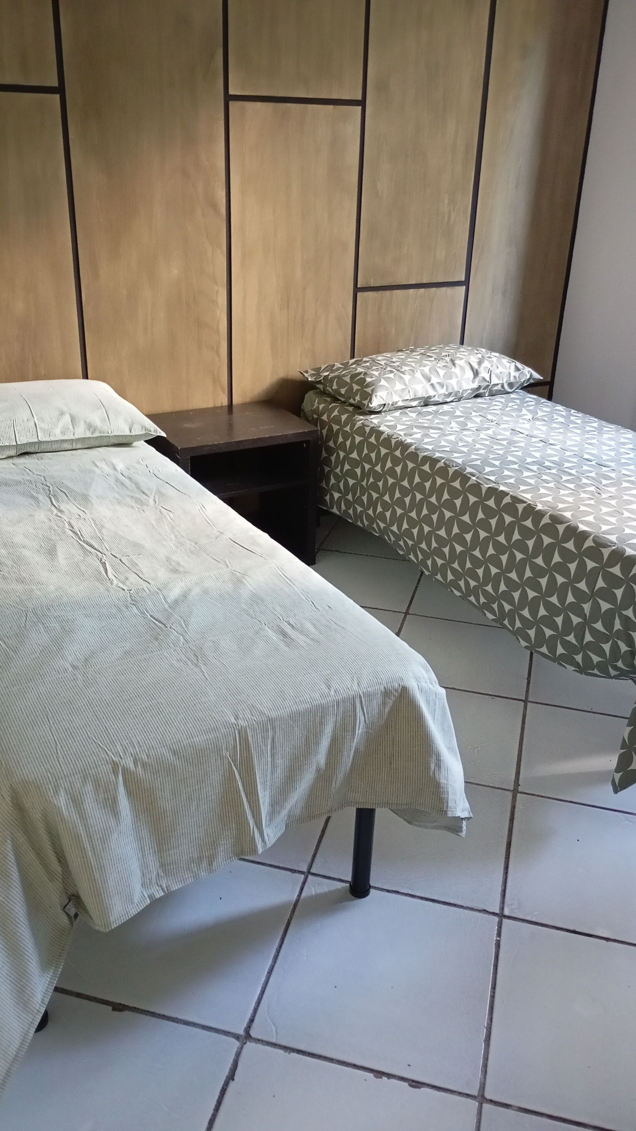 A bedroom with two beds, a wooden headboard, and a tiled floor.