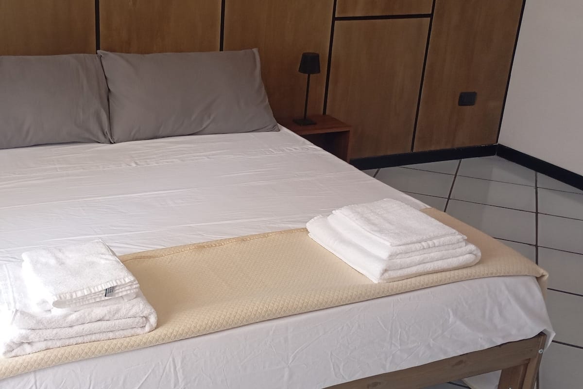 A neatly made bed with white linens, two pillows, and a beige blanket on a wooden bed frame.