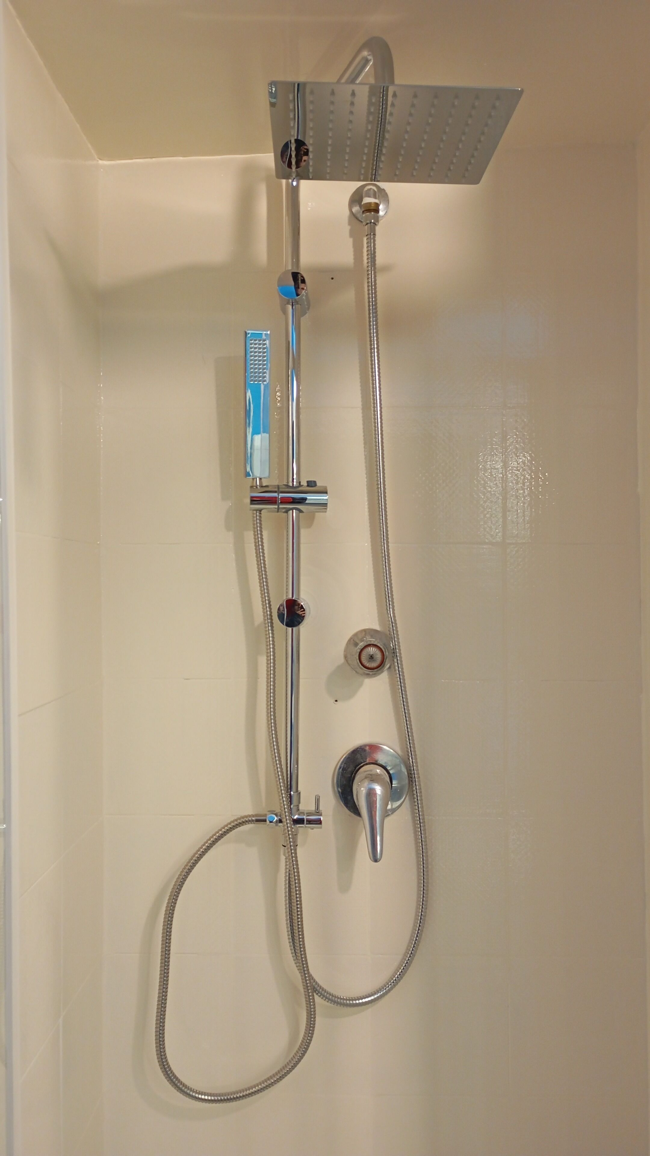 A shower with a handheld showerhead, a fixed showerhead, and a handheld shower hose.