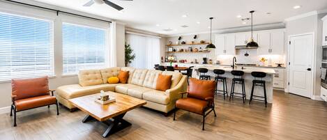 A modern living room with a sofa, chairs, a coffee table, and a kitchen area with bar stools.