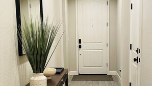 A hallway with a dark wooden console table, a potted plant, a white door, and a white door with a black handle. - Lovely Home in Lodi (Lodi)