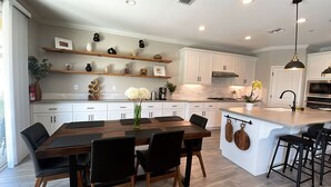 A modern kitchen with white cabinetry, a central island with bar stools, and decorative items on shelves. - Lovely Home in Lodi (Lodi)