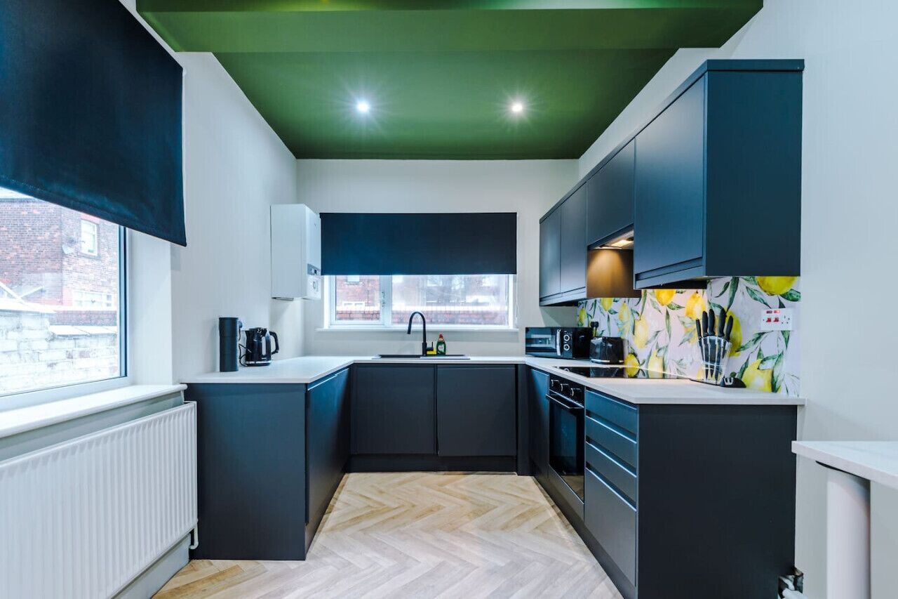 A modern kitchen with dark cabinetry, a herringbone wood floor, and a window with a view of the outside.