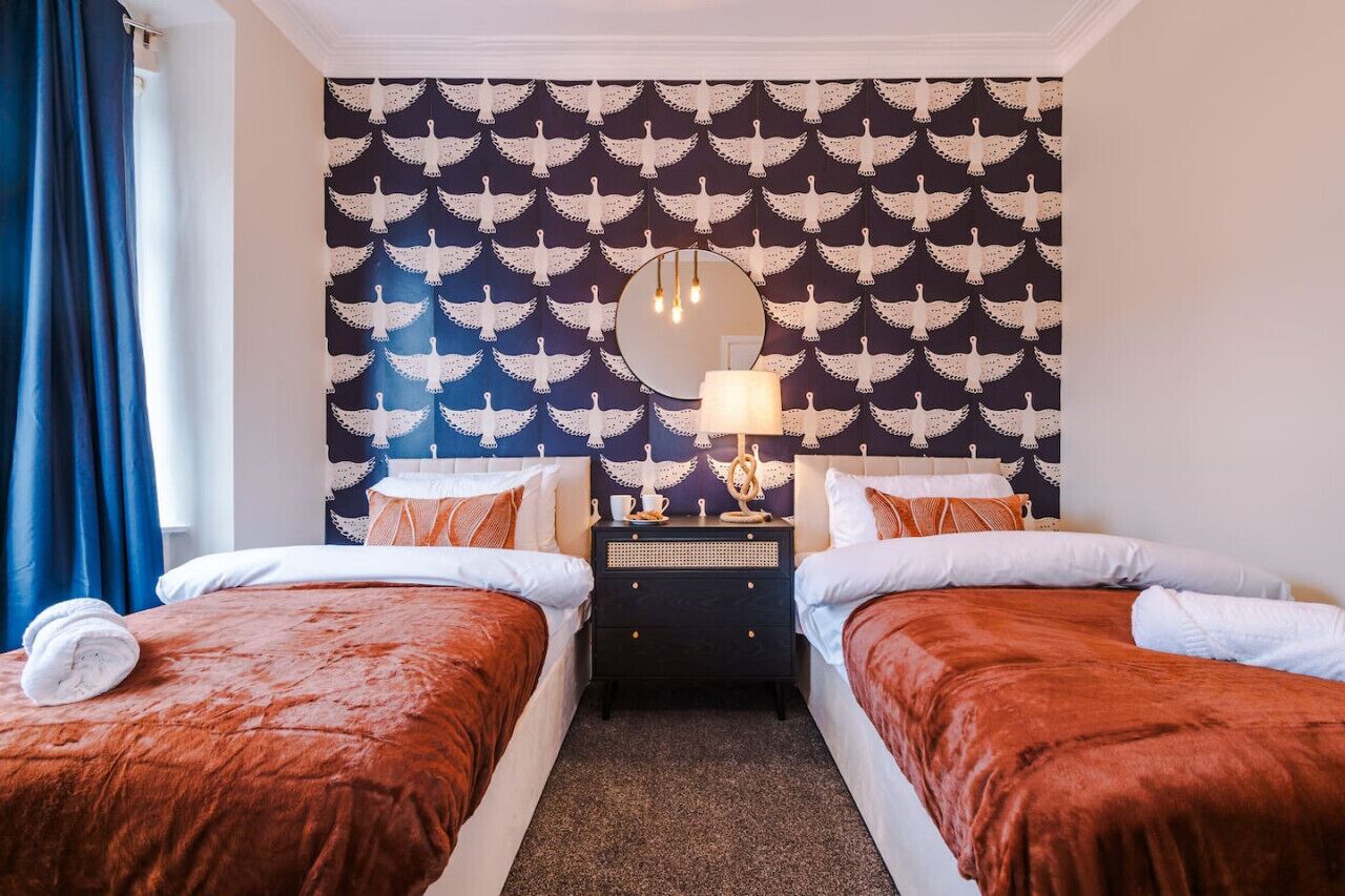 Ein Hotelzimmer mit zwei Betten, einem Nachttisch, einem Spiegel und einer Wand mit Taubenmuster.