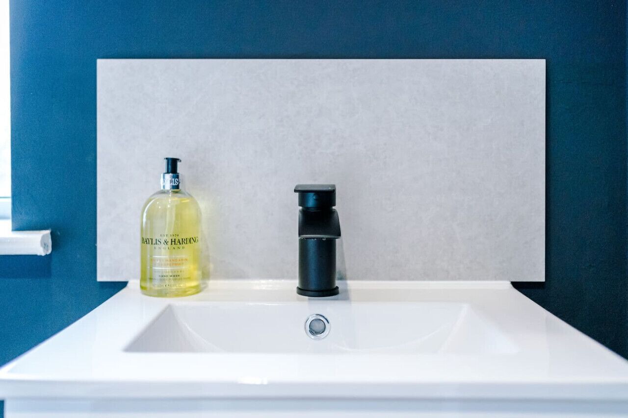 Un lavabo de salle de bain avec un flacon de savon liquide et un robinet noir.
