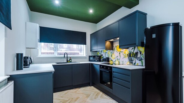 A modern kitchen with dark cabinetry, a black refrigerator, and a herringbone-patterned floor. - Salford Sanctuary 5 Bed House (Salford)