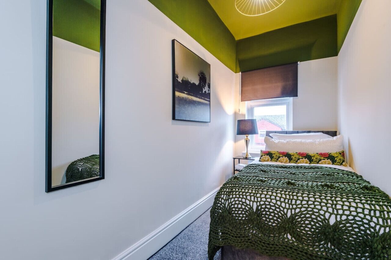 Une chambre à coucher comprenant un lit, une table de chevet, une lampe, une fenêtre et un miroir fixé au mur.