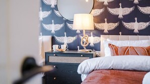 A bedroom with a bed, a bedside table with a lamp, and a wall with a bird pattern. - Salford Sanctuary 5 Bed House (Salford)