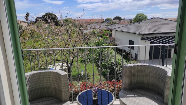 A balcony with wicker chairs, a glass table with flowers, and a view of a residential area with houses and trees. - Proche Mer, Appartement Classé 2 Dans Petite Résidence (Santa-Lucia-di-Moriani)
