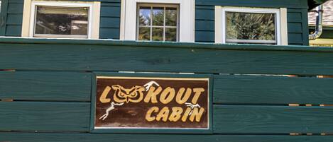 Een houten hutje met een bord waarop staat 'Lout Cabin'.