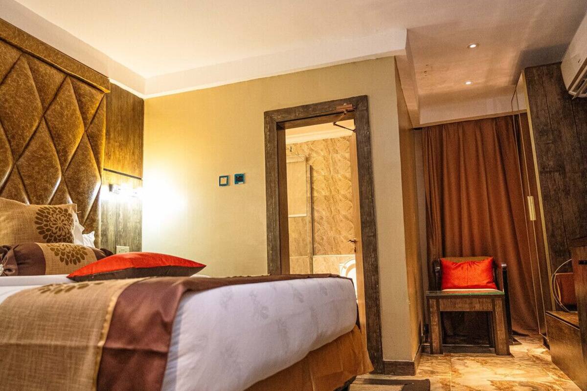 Una habitación de hotel con una cama grande, un cabecero de madera, un espejo, una silla y suelo de madera.