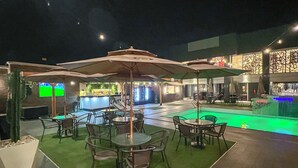 An outdoor seating area with tables and chairs, a pool, and a bar area.