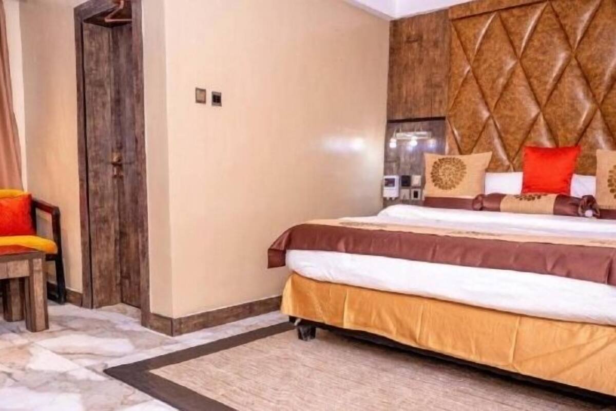 Una habitación de hotel con una cama grande, una puerta de madera y una silla con cojín.