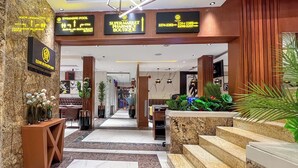 A hotel lobby with a marble floor, a reception desk, a staircase, and a sign indicating a swimming pool.