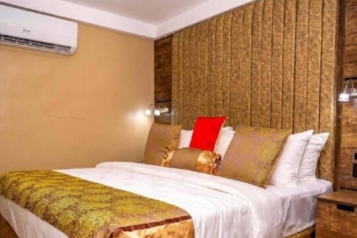 Habitación de hotel con una cama, cabecera de madera, almohada roja y aire acondicionado montado en la pared.