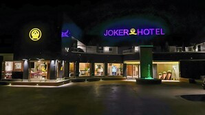 The exterior of the Joker Hotel at night with illuminated signage and a well-lit entrance.