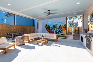 Et moderne udeområde med en hjørnesofa, træborde og et muralmaleri på væggen.