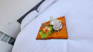 Un letto rifatto con lenzuola bianche, un vassoio di legno con croissant e una tazza di caffè, e un piccolo oggetto decorativo sul letto.