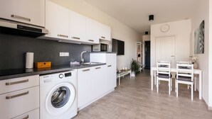 Una cucina moderna con mobili bianchi, lavatrice integrata e zona pranzo con tavolo e sedie.