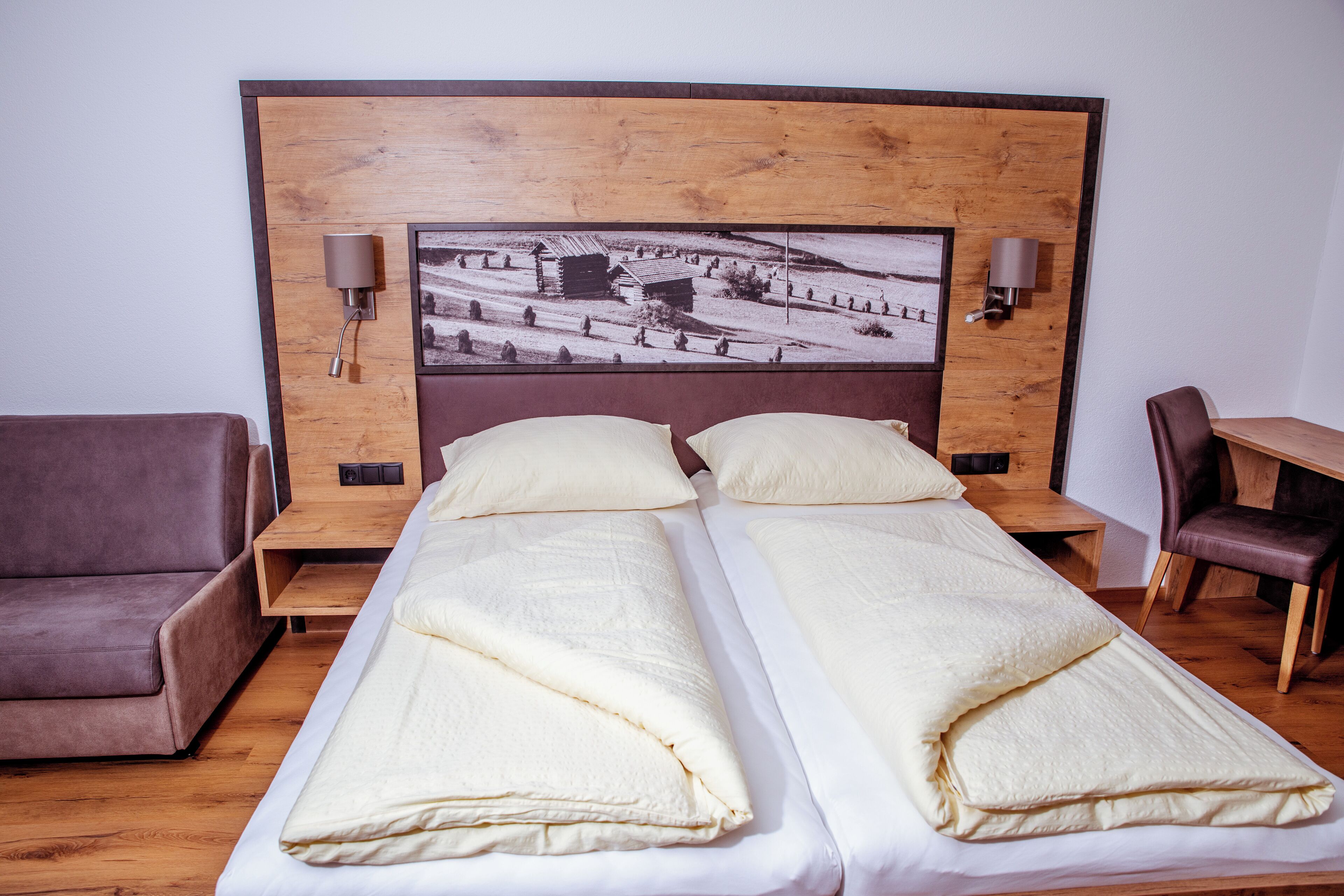 Una cama doble con cabecera de madera, dos mesitas de noche, un sofá de cuero marrón y un escritorio de madera con una silla.