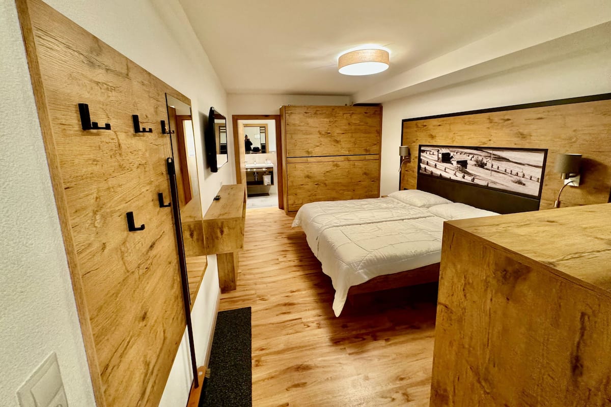 A bedroom with a wooden headboard, a bed with white bedding, a wooden dresser, and a mirror.