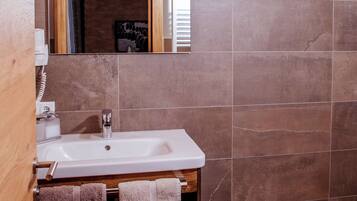 A bathroom with a wooden ceiling, a white sink, a mirror, and brown tiles.