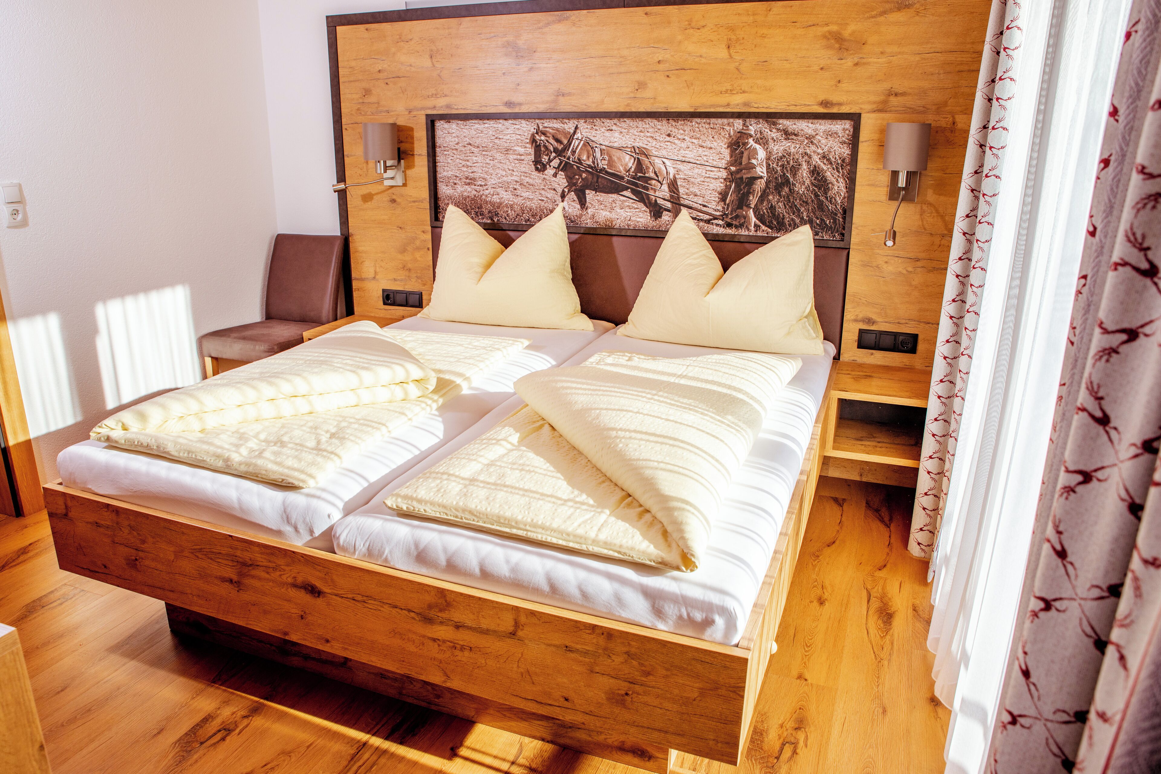 A wooden bed with two pillows and a headboard with a picture of a horse-drawn cart.