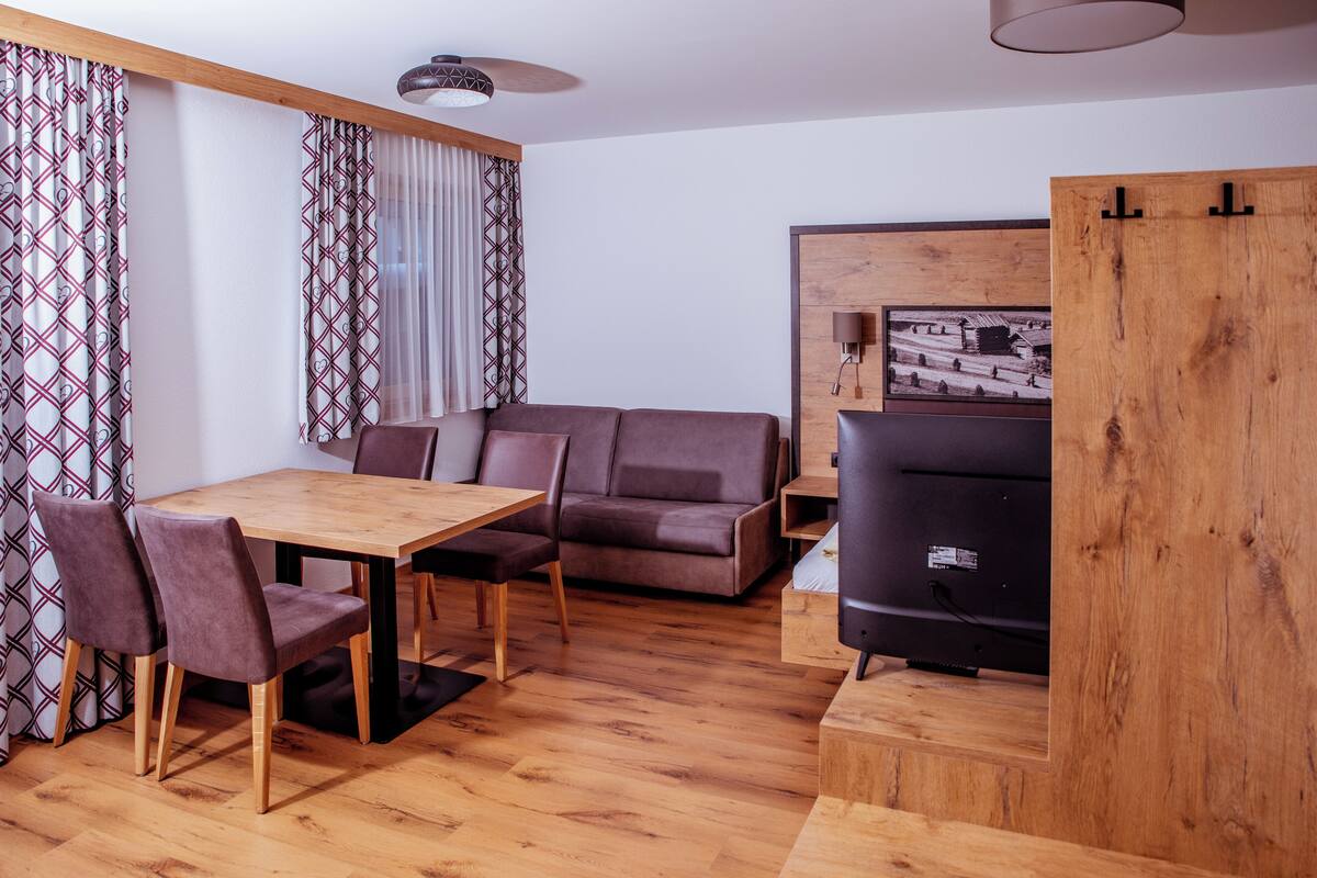 A modern living room with a wooden dining table, two sofas, and a TV.