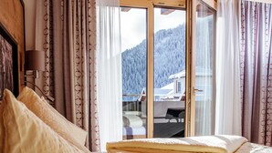A bedroom with a large bed, wooden ceiling beams, and a view of a mountain through a window. - Apart Darre (Serfaus)